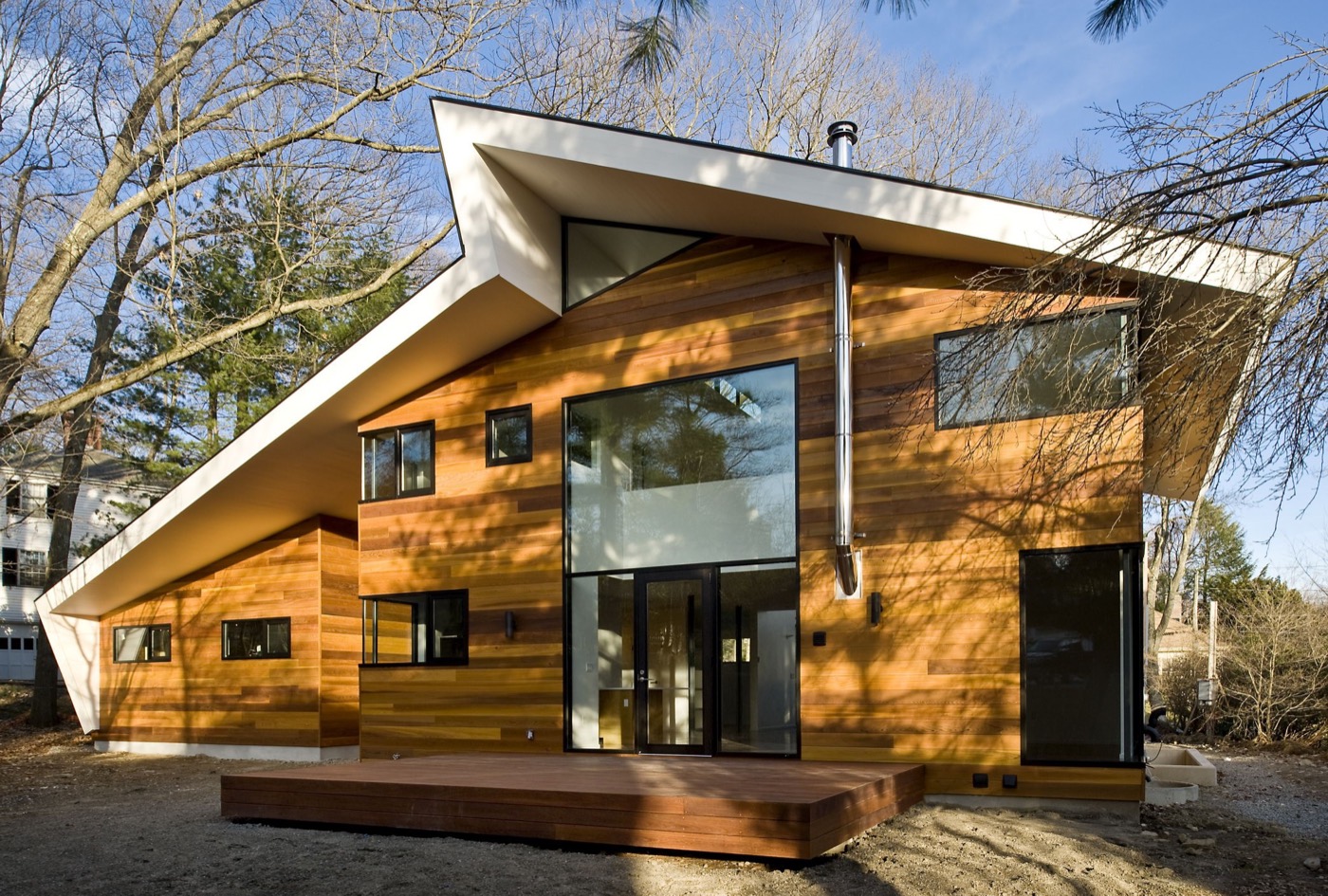 Rear of the house in daylight: a two-storey glazed wall with black-framed doors, cedar siding, an ipe deck, the white roof overhanging deeply