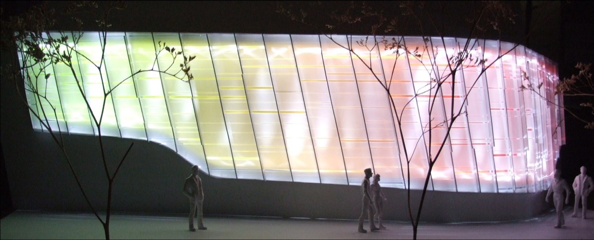 A backlit physical model at night: a curved translucent wall glowing green to pink between vertical mullions, scale figures and wire trees in front