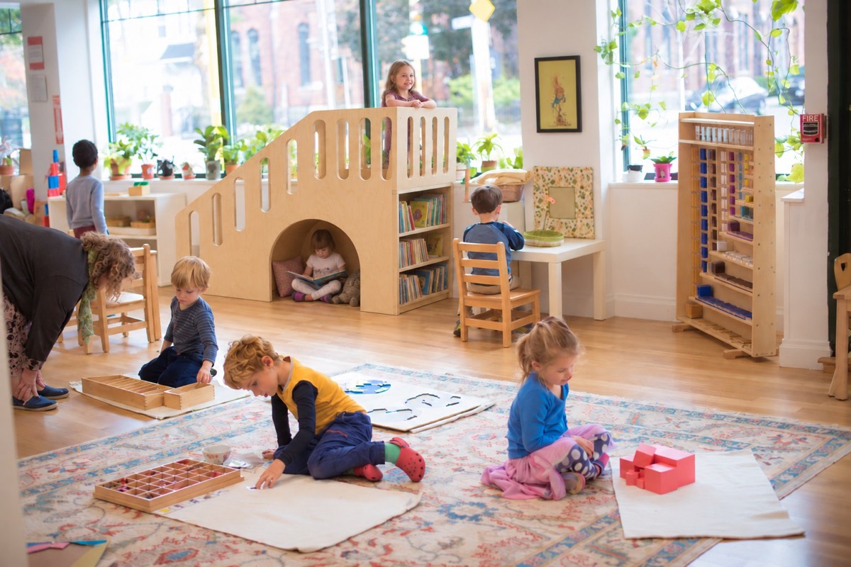 A rendering of the plywood play stair placed against the windowed wall of the classroom, children on rugs around it