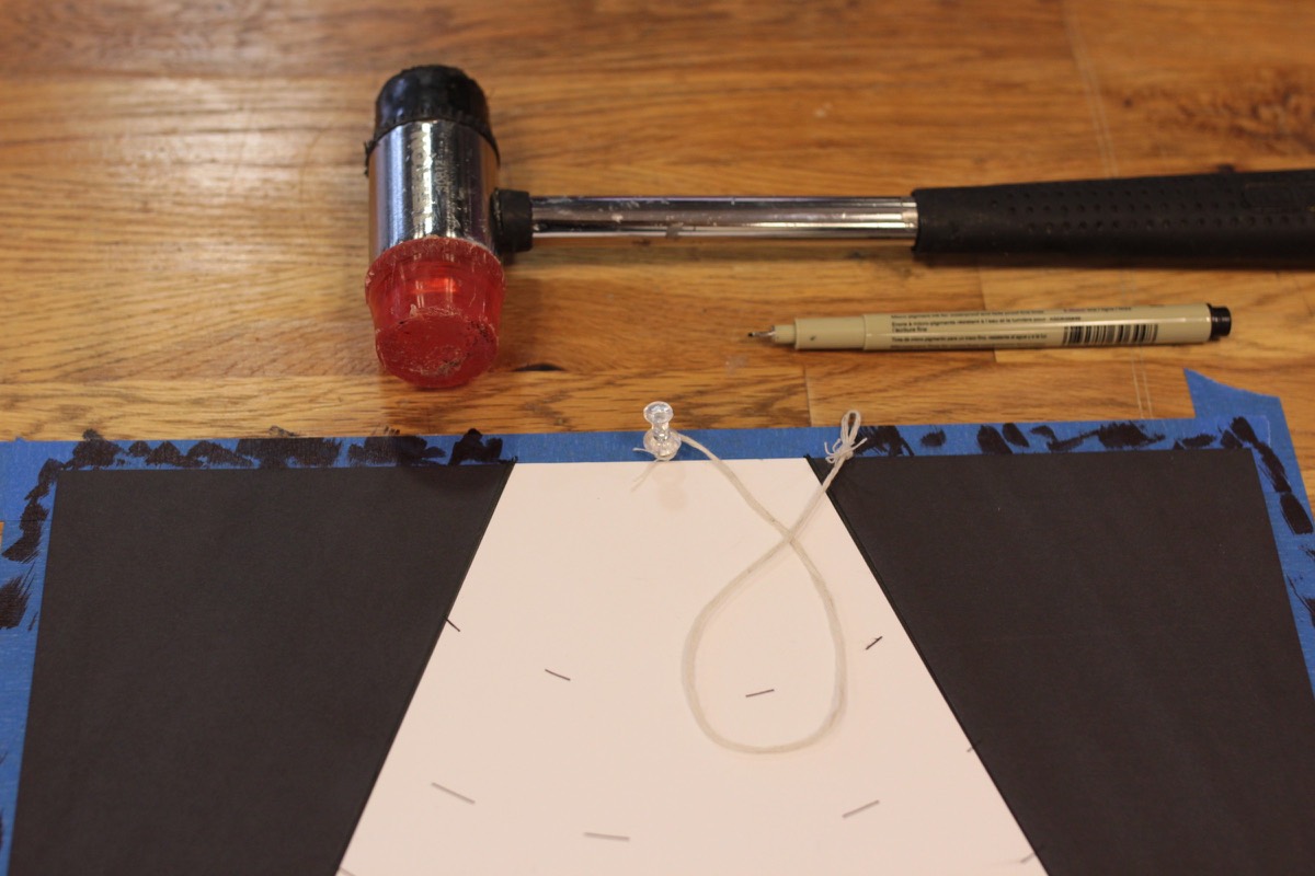 A rubber mallet and a pen on a wood table beside a taped-down sheet with a white wedge form