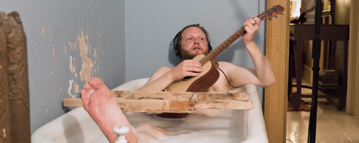 A man in a bathtub playing a guitar in a peeling room