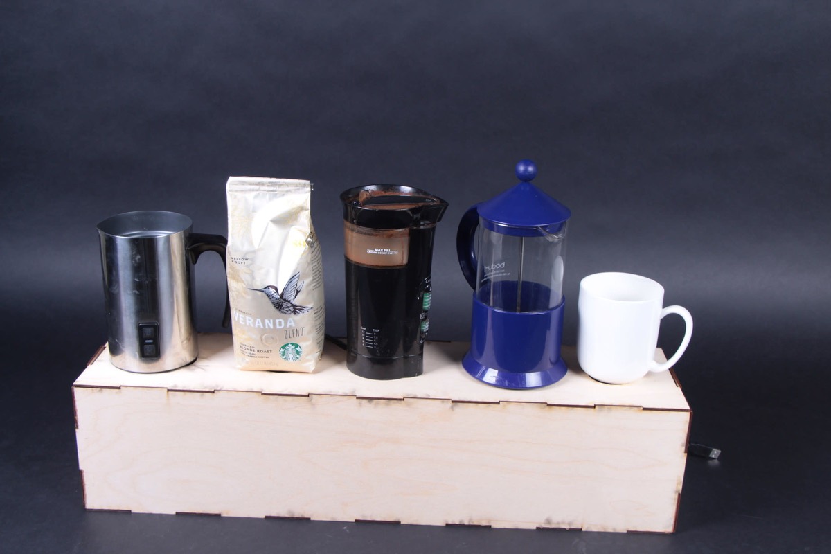 A plywood table with a kettle, a bottle, a mug, and a striker mechanism on it