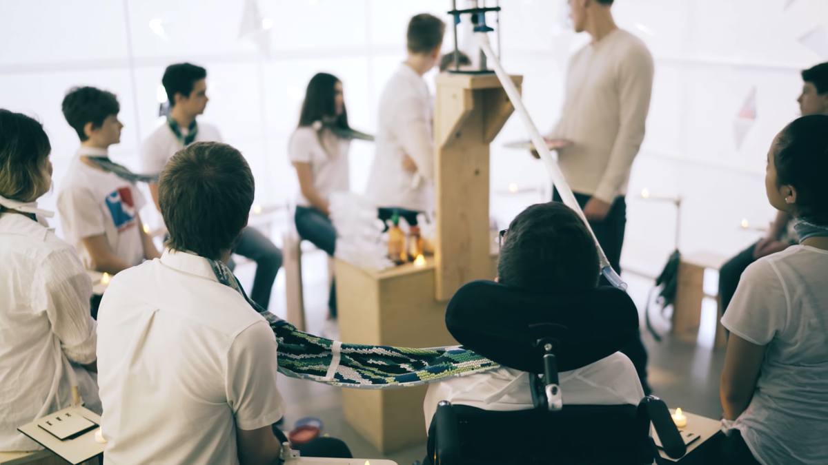 Students in white seated in a circle around a wooden tower, Lee at the centre